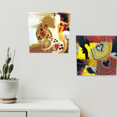 Duas pinturas abstratas coloridas com corações penduradas numa parede branca, cacto em vaso branco em superfície branca