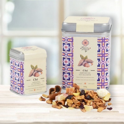 Duas caixas metálicas de chá com padrão colorido e chá solto com frutos secos em superfície de madeira