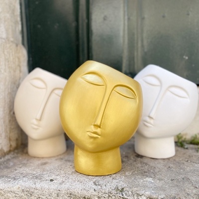 Três vasos decorativos em forma de rosto estilizado, dois creme e um dourado