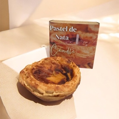 Vela em forma de pastel de nata com caixa ao fundo.