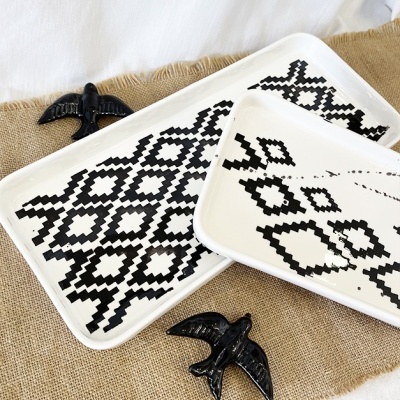 Três tabuleiros brancos com padrão preto e pássaros cerâmicos pretos sobre tecido de juta