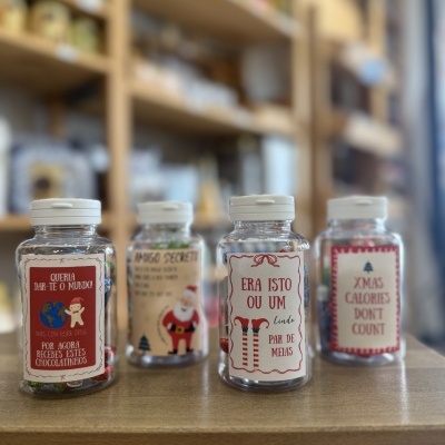 Frascos transparentes com chocolates e etiquetas natalícias em prateleira de loja