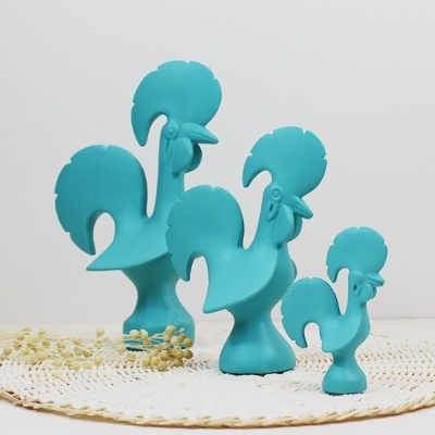 Três esculturas de galo azul turquesa sobre um tapete branco tecido.