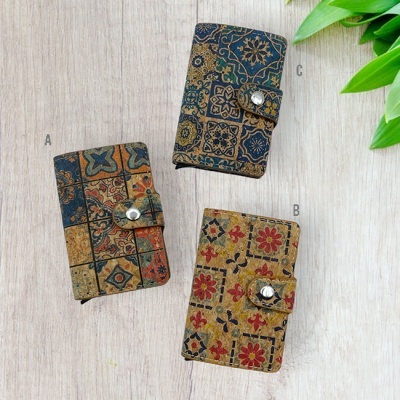 Três carteiras ou porta-cartões coloridos com padrões de azulejos em superfície de madeira clara e folhas verdes