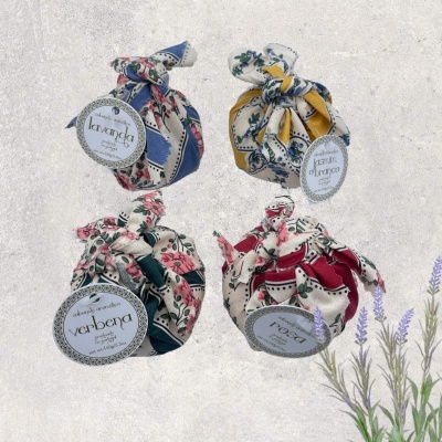 Quatro sacos pequenos de tecido estampado com etiquetas redondas, fundo cinza claro e ramo de lavanda.