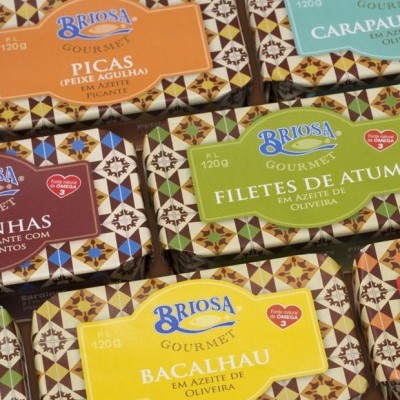 Latas de conservas Briosa Gourmet de vários peixes com rótulos coloridos e padrão geométrico no fundo