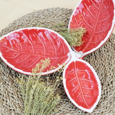 Travessas vermelhas em forma de folhas com bordas brancas sobre base trançada castanha com flores secas