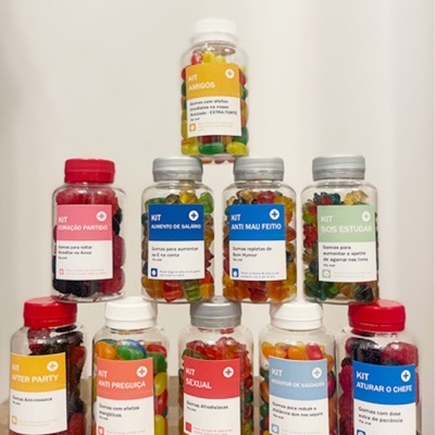 Dez frascos de gomas jelly beans coloridas empilhados em pirâmide com etiquetas coloridas em português sobre fundo branco