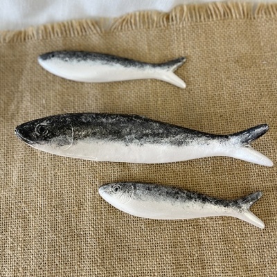 Três peixes decorativos de cerâmica cinza e branco sobre tecido de juta