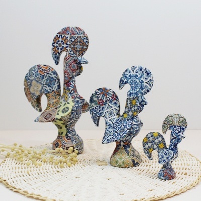 Figuras de galo em cerâmica colorida com padrões de azulejos em cima de tapete de crochê