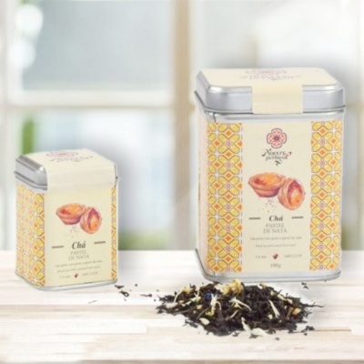 Duas latas metálicas de chá com rótulos decorados amarelos e laranjas e chá solto em superfície clara