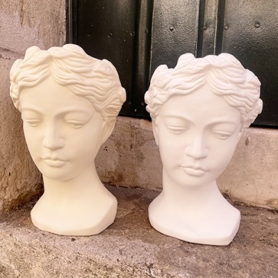 Dois bustos de esculturas femininas em tons creme claro e branco sobre pedra