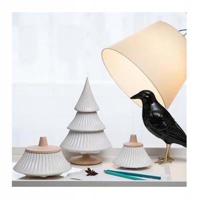 Conjunto decorativo cerâmico com árvore de Natal e pássaro preto sobre mesa branca com candeeiro