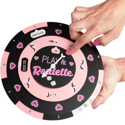 Jogo de tabuleiro redondo rosa e preto com texto PLAY & Roulette e dados, com mãos femininas a girar.