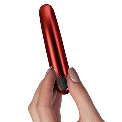 Mão segurando vibrador pequeno vermelho metálico com botão preto