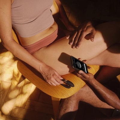 Pessoa sentada em cadeira de madeira com roupa interior rosa e outra pessoa segurando dispositivo eletrônico preto