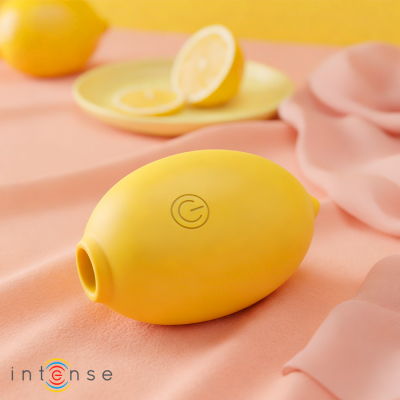 Dispositivo amarelo em forma de limão com botão de ligar, sobre tecido rosa, com limões ao fundo.