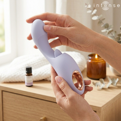 Vibrador lilás com detalhes dourados rosé segurado por mãos femininas sobre mesa de madeira