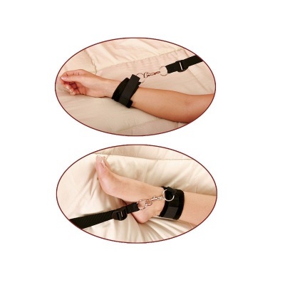 Algemas de tecido preto presas ao pulso e tornozelo com correias e ganchos metálicos, sobre superfície bege