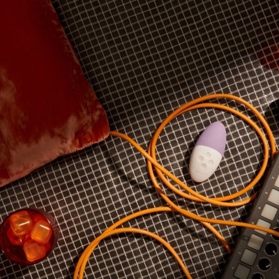 Distribuição de almofada vermelha, cabo laranja, controlador roxo e branco e dispositivo eletrônico sobre superfície quadriculada.