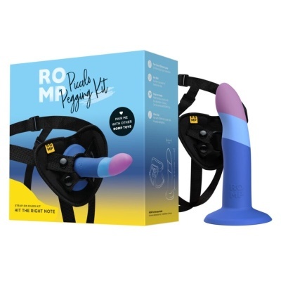 Kit de pegas ROMP Piccolo com dildo bicolor em silicone e cinto preto ajustável ao lado da caixa azul e amarela