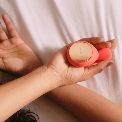 Frasco de perfume Le Labo vermelho e dourado nas mãos sobre tecido branco