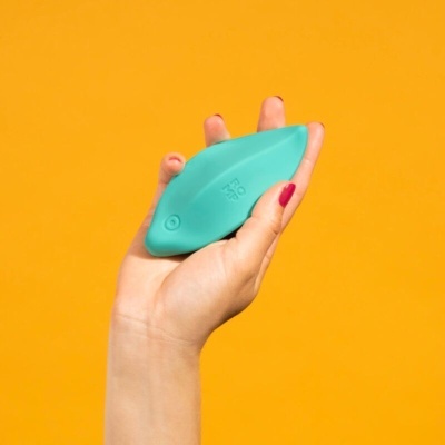 Objeto azul em forma de peixe com texto RO ME numa mão com fundo laranja
