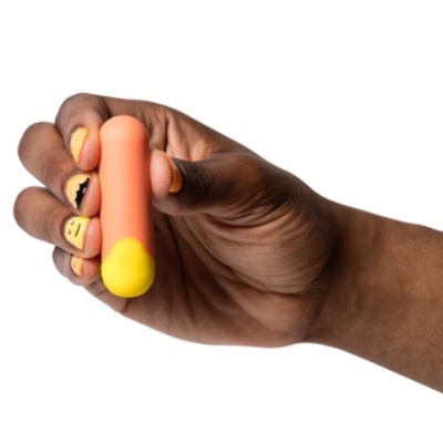 Mão com objeto oval laranja e amarelo com unhas pintadas amarelas e desenhos pretos