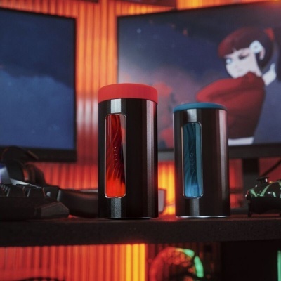 Altifalantes cilíndricos preto com vermelho e azul numa mesa com ecrãs ao fundo