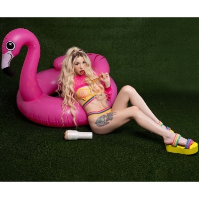 Mulher loira de biquíni junto a boia insuflável rosa flamingo na relva artificial