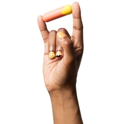 Mão segurando objeto oval laranja com ponta amarela, unhas amarelas com desenhos