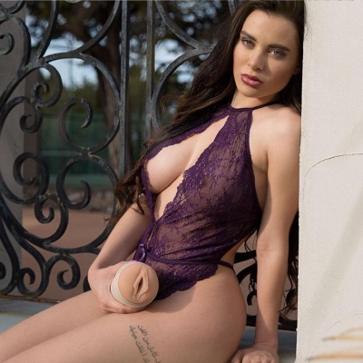 Mulher com lingerie de renda roxa sentada junto a muro branco e grade de ferro decorativa