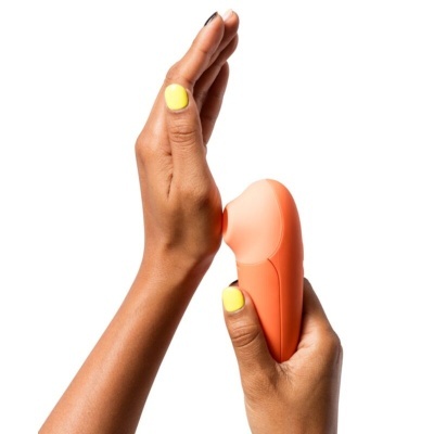 Aparelho portátil coral segurado por mão com unhas amarelas em fundo branco