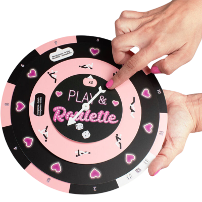 Jogo de tabuleiro redondo rosa e preto com texto PLAY & Roulette e dados, com mãos femininas a girar.