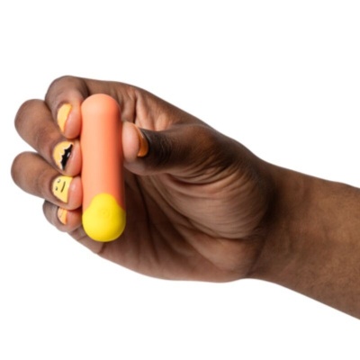 Mão com objeto oval laranja e amarelo com unhas pintadas amarelas e desenhos pretos