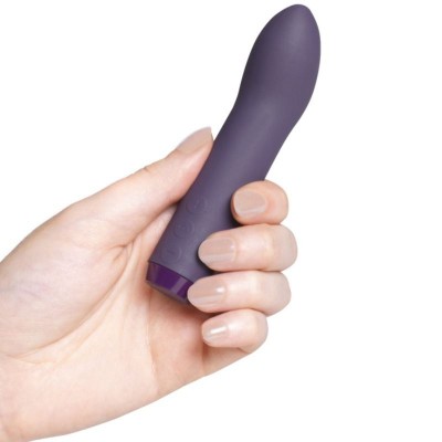 Mão segurando vibrador roxo pequeno com fundo branco