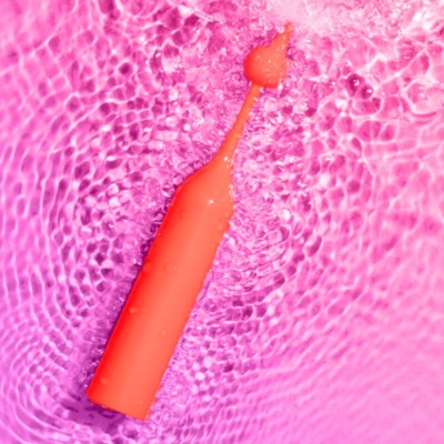 Vibrador pessoal laranja sobre superfície rosa ondulada