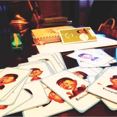 Cartas com ilustrações de expressões faciais e palavras em português sobre uma mesa com caderno e estojo verde