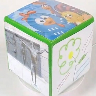 Cubo macio com faces ilustradas e desenhos coloridos de personagens, flor e figuras humanas em relevo.