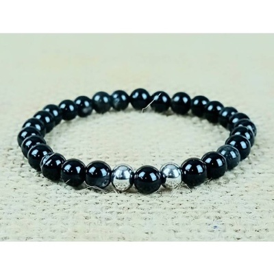 Pulseira de contas pretas com três contas prateadas no centro sobre tecido bege