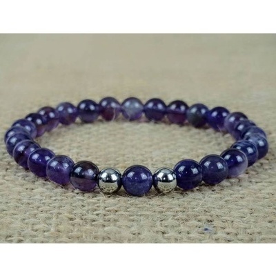 Pulseira de contas roxas e metálicas sobre tecido bege