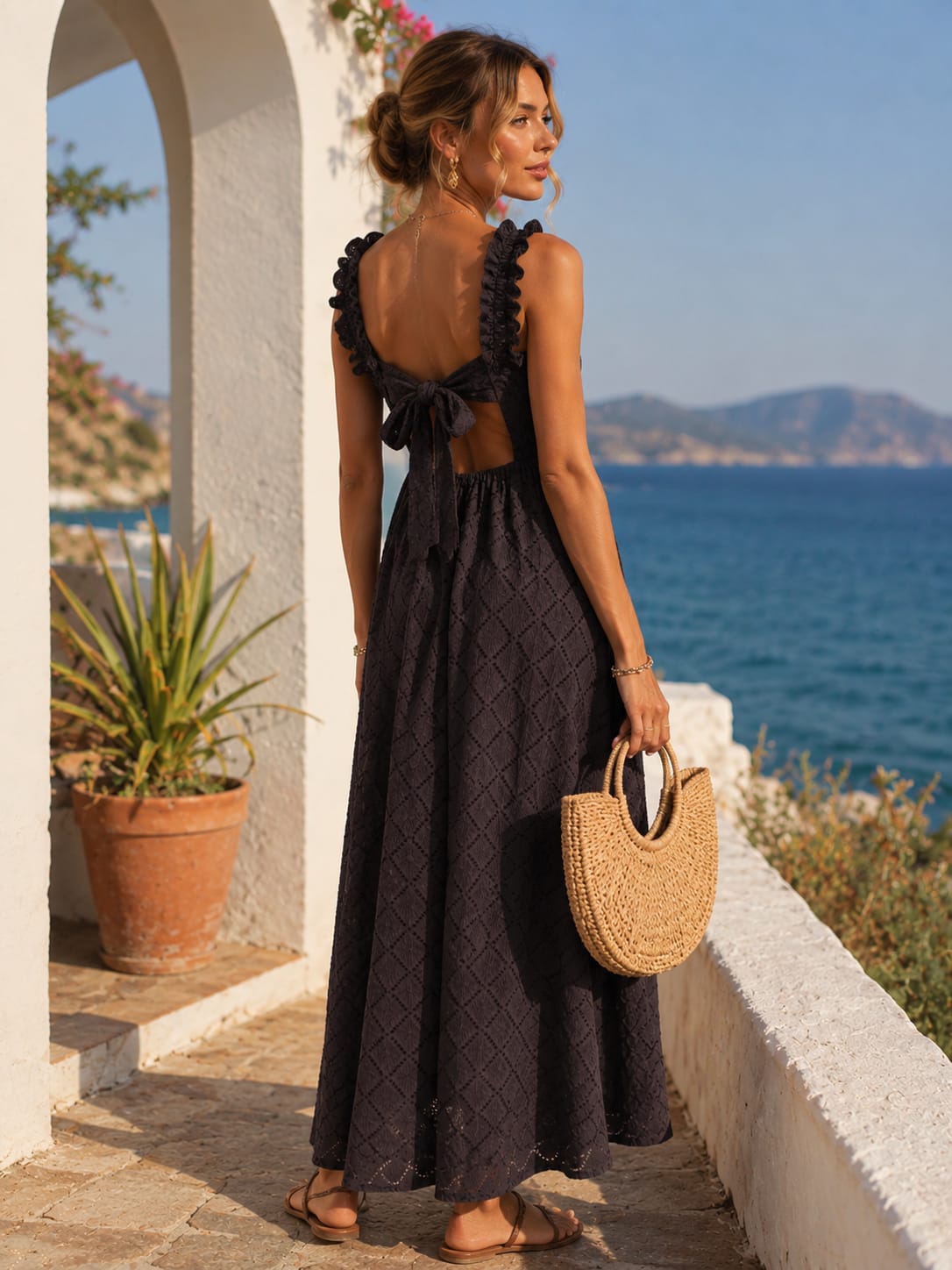 Vestido Susana Mulher vista de costas com vestido preto longo e mala de palha junto ao mar