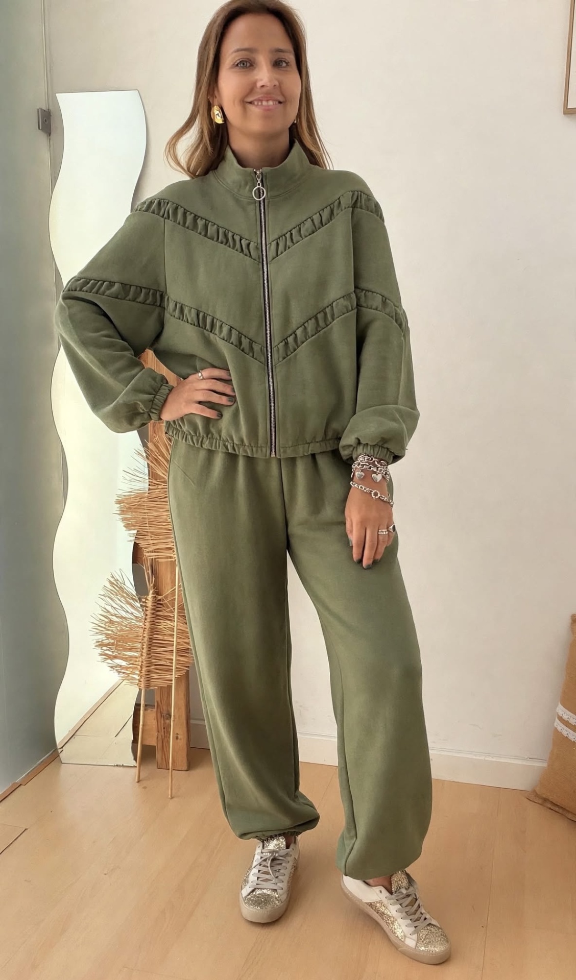 Conjunto Laura Conjunto verde musgo com casaco e calças largas, mulher com pulseiras prateadas e ténis brancos com detalhes brilhantes.