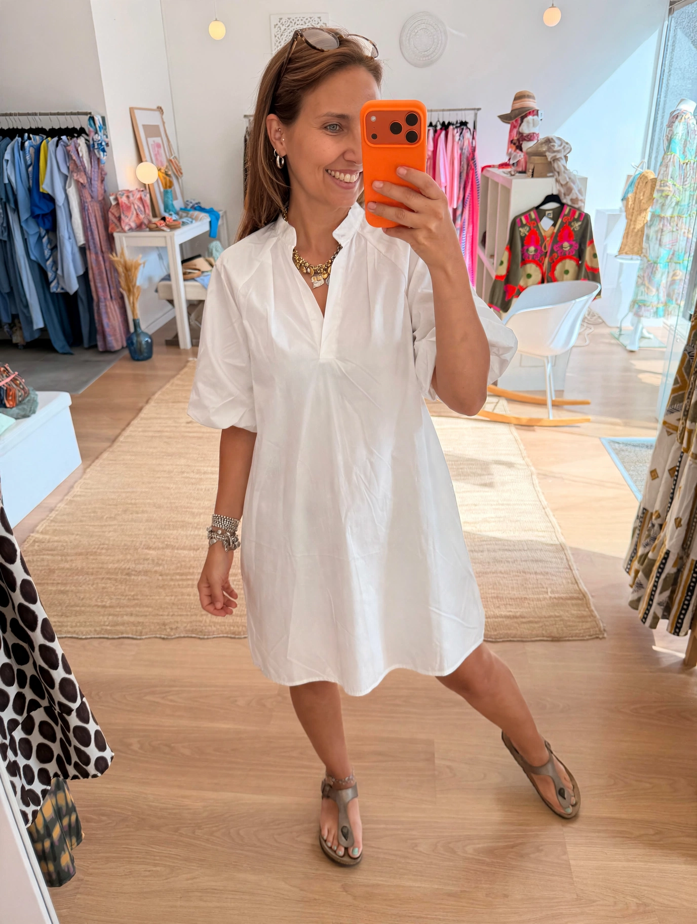 Vestido Lili Vestido branco de manga curta com gola alta num cenário de loja de roupa.
