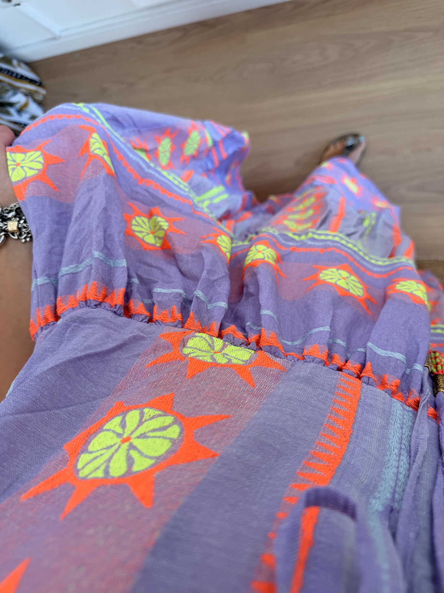 Vestido Boho Chic Fluo Vestido ou saia lilás com bordados em néon laranja e verde, vista de cima sobre chão de madeira