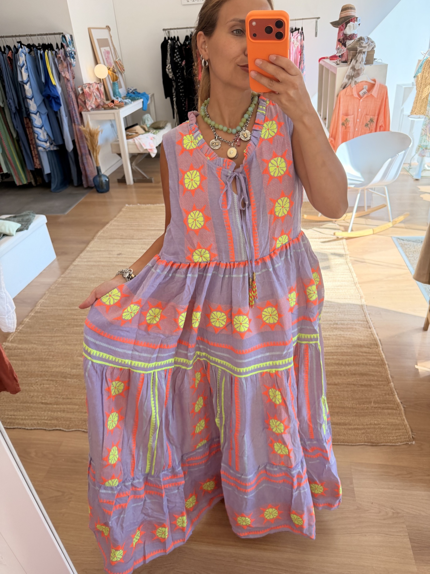 Vestido Boho Chic Fluo Vestido lilás com flores amarelas e detalhes laranja mostrado numa selfie de corpo inteiro em loja de roupa.