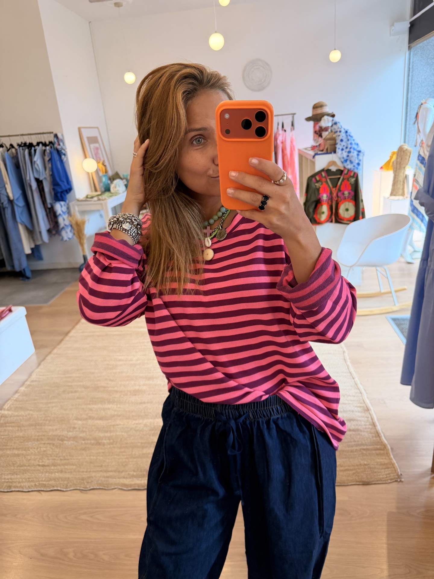 Camisola Riscas Blusa às riscas rosa e roxa com calças azul-escuras em selfie numa loja de roupa