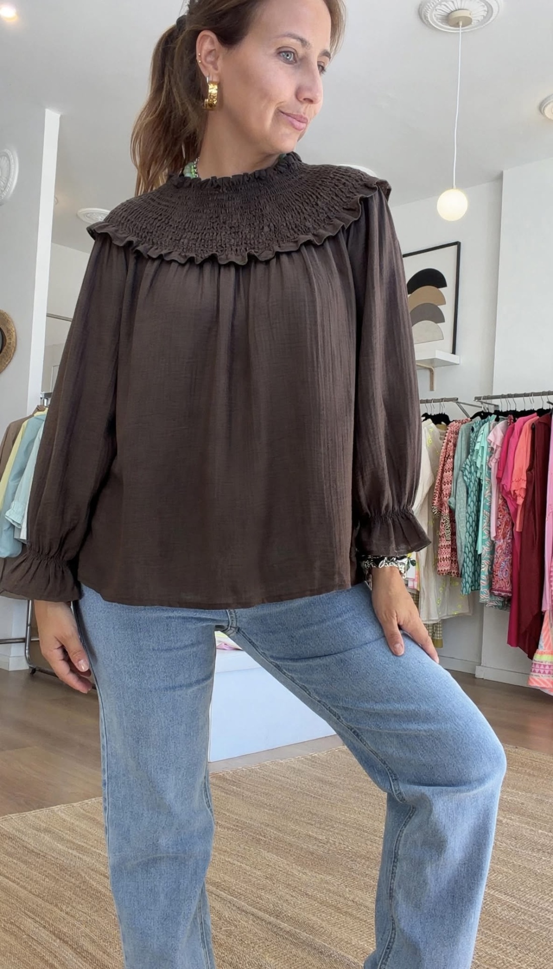 Blusa 2 em 1 Blusa castanha com gola e punhos franzidos, jeans azuis claros e roupas ao fundo