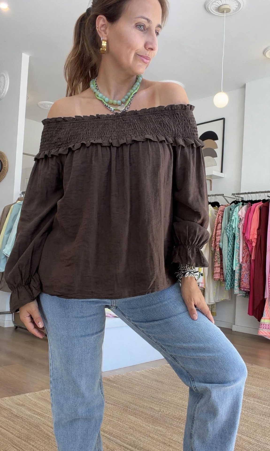 Blusa 2 em 1 Blusa castanha ombro a ombro com folhos e jeans azuis claros usada por mulher