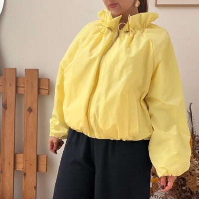 Mulher de casaco amarelo e calças pretas em ambiente interior com decoração simples